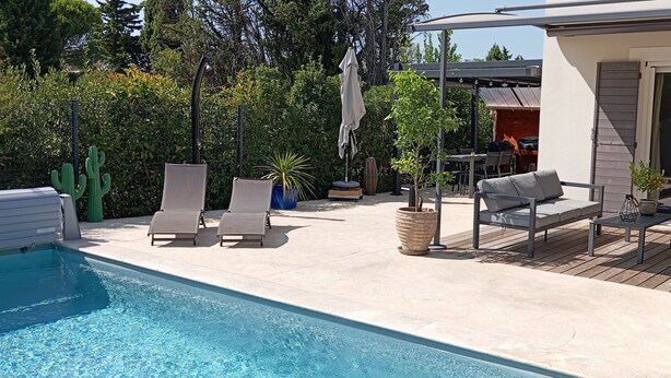 Un espace aménagé au bord de la piscine, avec des chaises longues, une table et un barbecue.