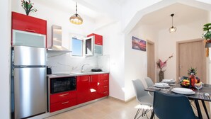 A modern kitchen with red cabinets, stainless steel appliances, and a dining area with a table set for two.