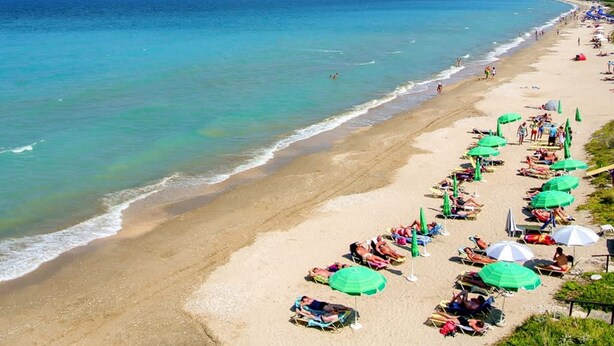 A beach with rows of sunbeds and umbrellas along the shoreline.