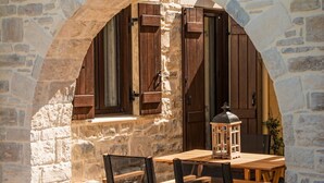 Un arco de piedra que da paso a una mesa y sillas de madera en un patio.