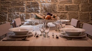 Mesa de comedor preparada con platos, vasos y cubiertos, frente a una pared de piedra con una lámpara colgante.