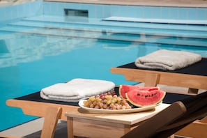 A poolside setting with a table holding a plate of grapes and watermelon slices, and two towels on lounge chairs. - Phaistos Villas - Villa Kastalia Poolside Retreat (Faistos)