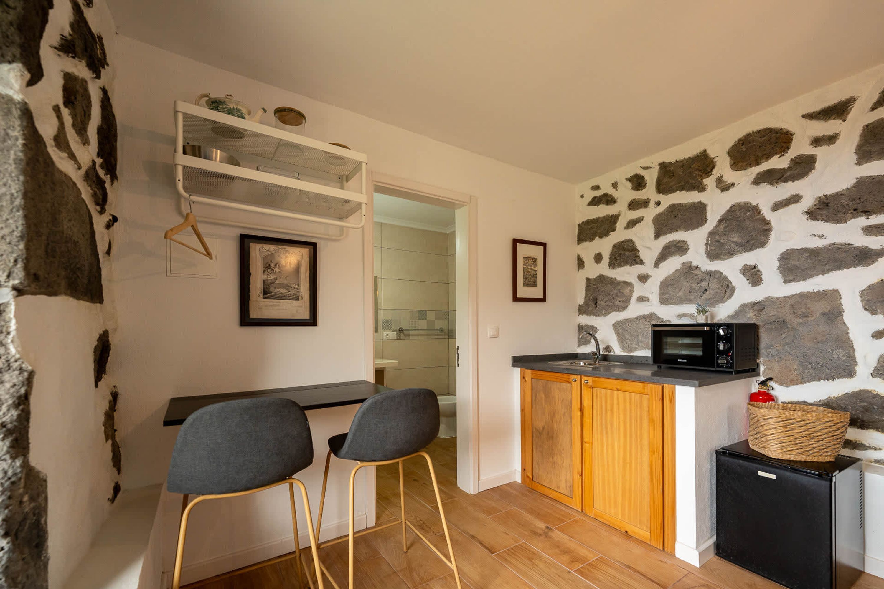 A compact kitchen with a stone wall, a microwave, a small refrigerator, and a wooden cabinet.