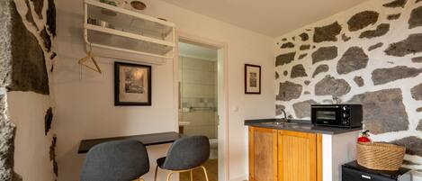 A compact kitchen with a stone wall, a microwave, a small refrigerator, and a wooden cabinet.