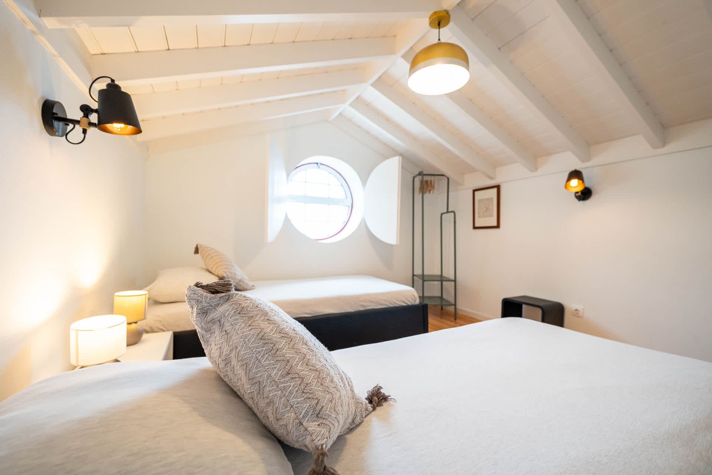 Une chambre avec deux lits, une fenêtre et un plafond avec des poutres apparentes.