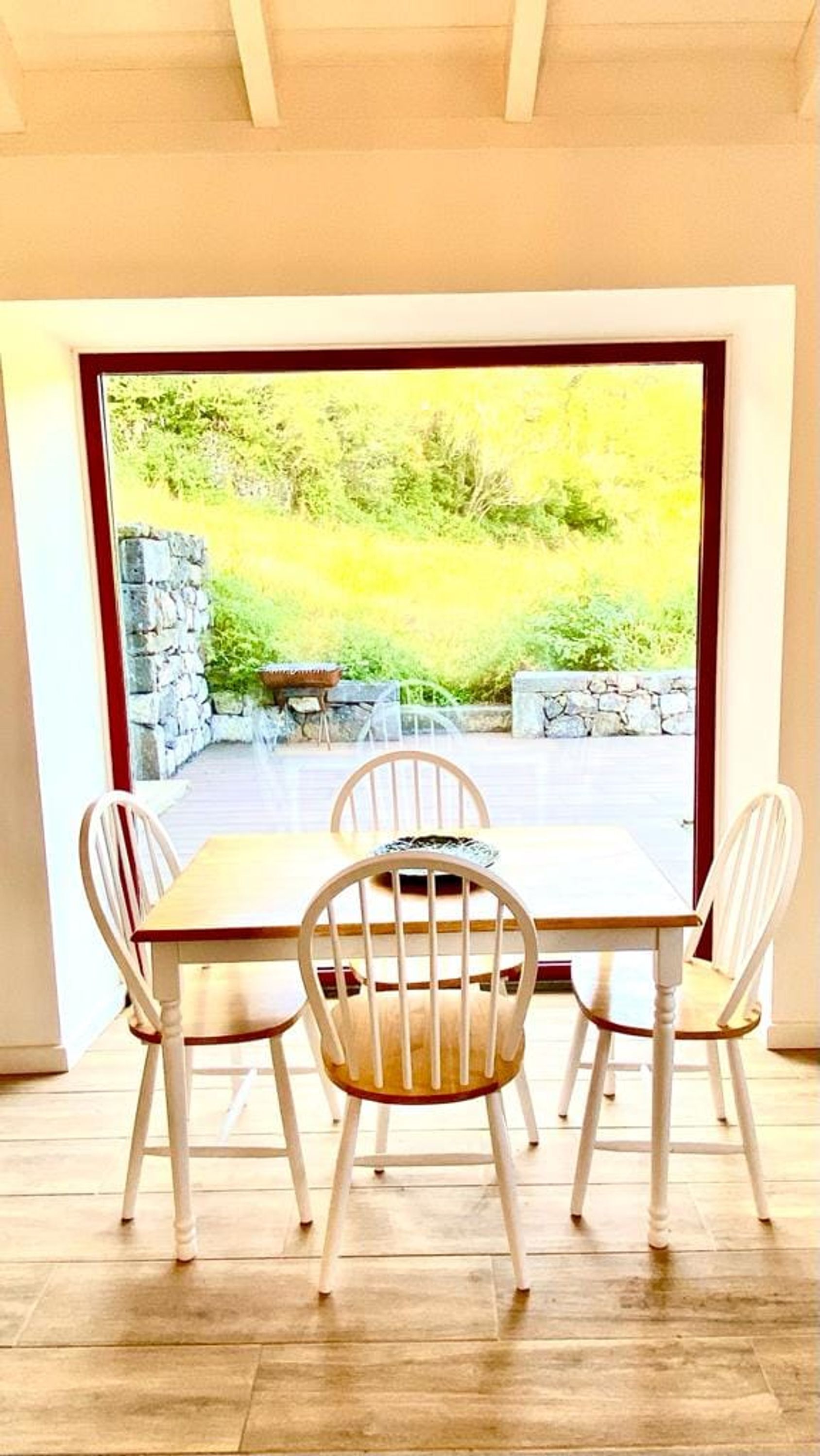 Zona pranzo con tavolo e quattro sedie, parete in pietra e vista su un giardino.