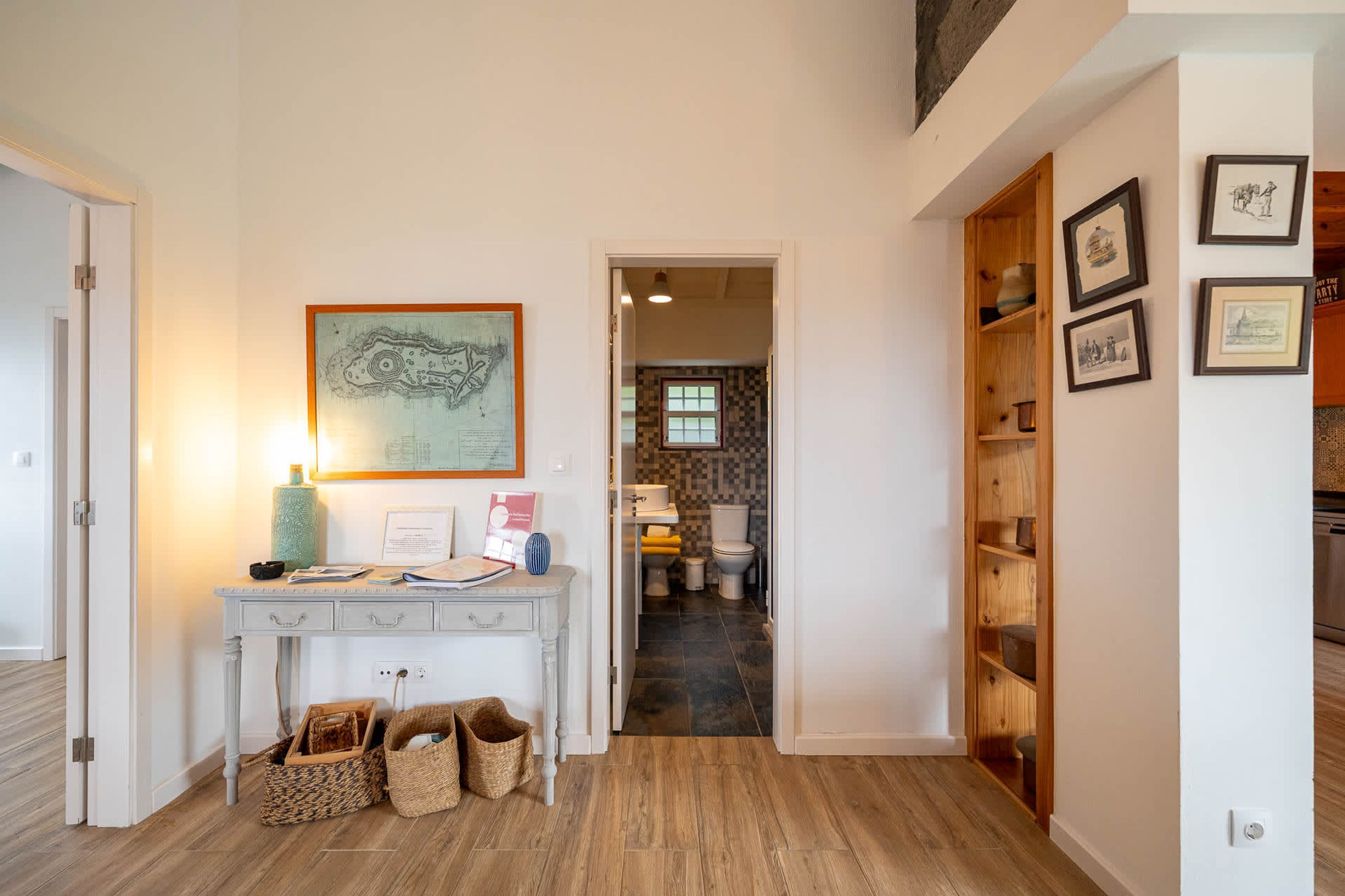 A hallway with a console table, baskets, a framed map, and a wooden shelving unit with framed pictures.