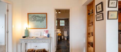 A hallway with a console table, baskets, a framed map, and a wooden shelving unit with framed pictures.