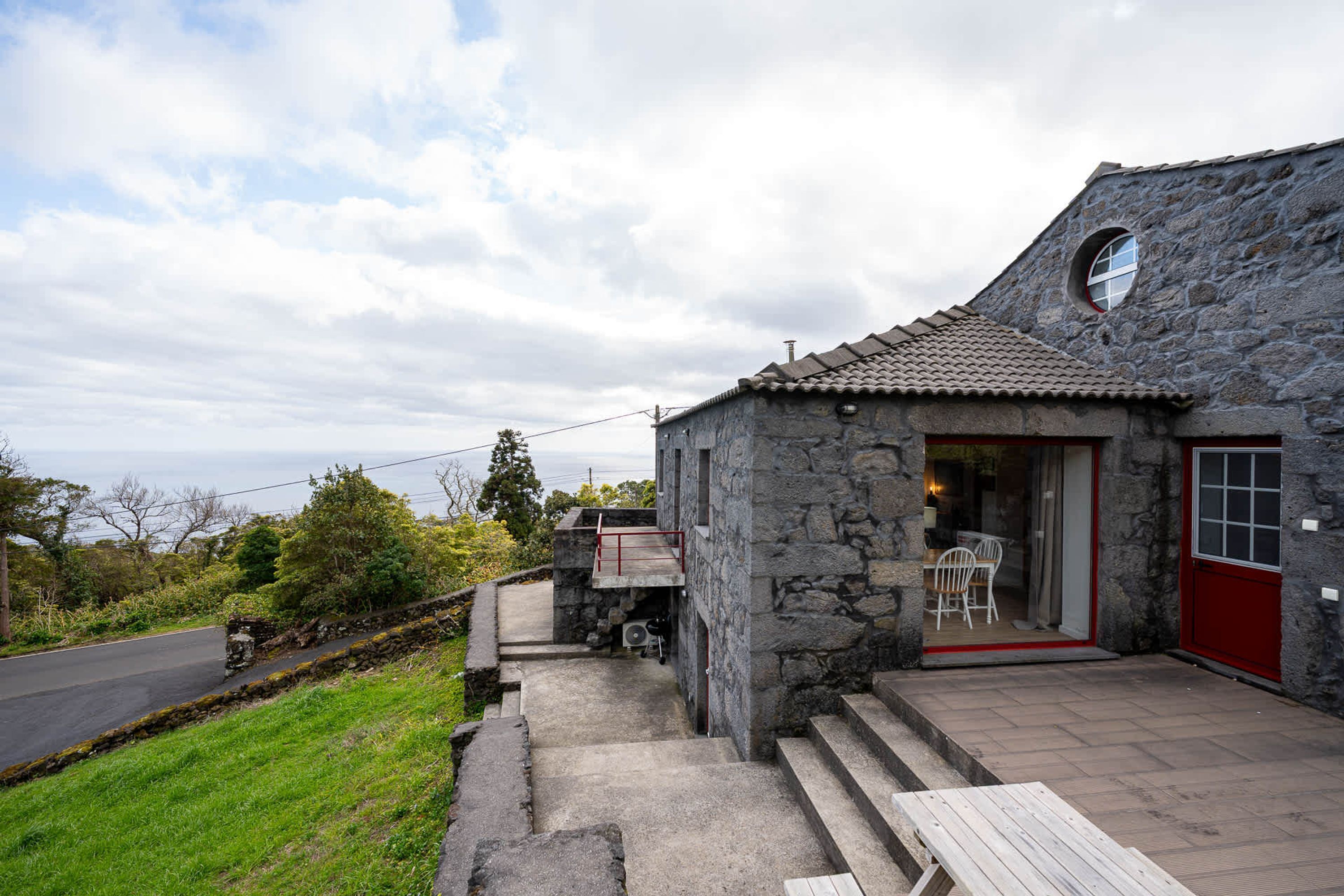 Una casa de piedra con puerta roja, un pequeño patio y vista al mar.