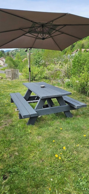 Una mesa de picnic con toldo en un área verde con árboles y casas al fondo.