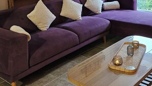 Una sala de estar con un sofá morado, una mesa de centro de madera y una estantería de madera rústica.
