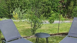 Tres sillones de descanso y una mesita redonda en un área verde al aire libre, con árboles al fondo.