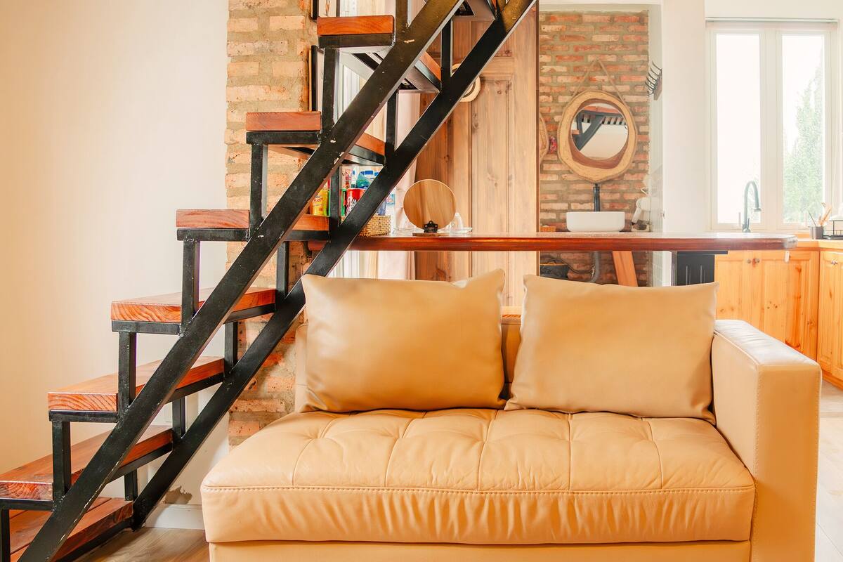 A modern living room with a sofa, a wooden staircase, and a kitchen area.