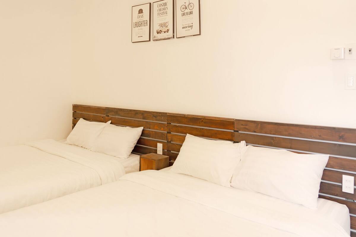A double bed with a wooden headboard, two bedside tables, and three framed posters on the wall.