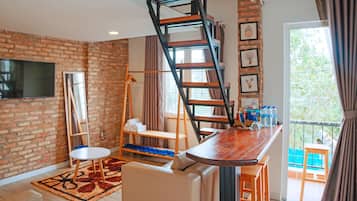 A room with a brick wall, a wooden ladder, a TV, a sofa, a small table, and a window with a view.