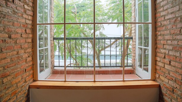 Quarto com uma grande janela dividida em várias partes, paredes de tijolo e vista para árvores e um corpo d'água.