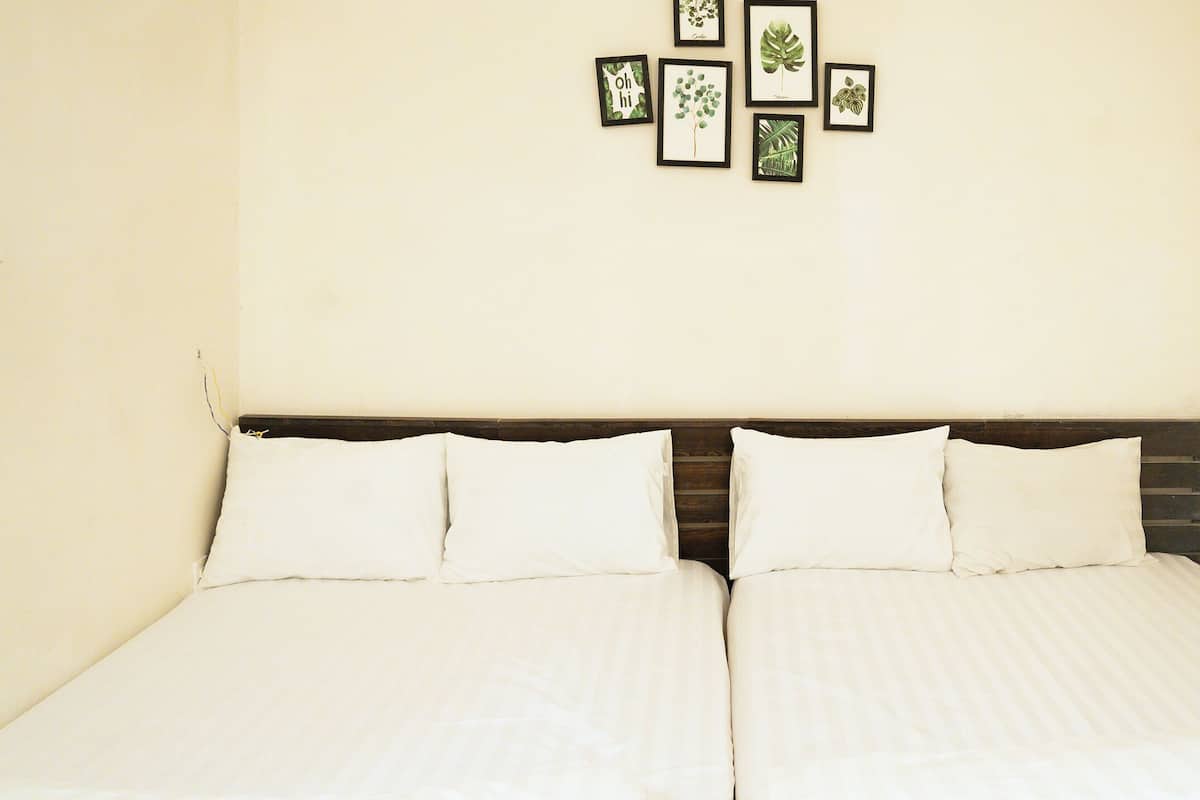 A double bed with white bedding, a wooden headboard, and a wall with framed botanical prints.