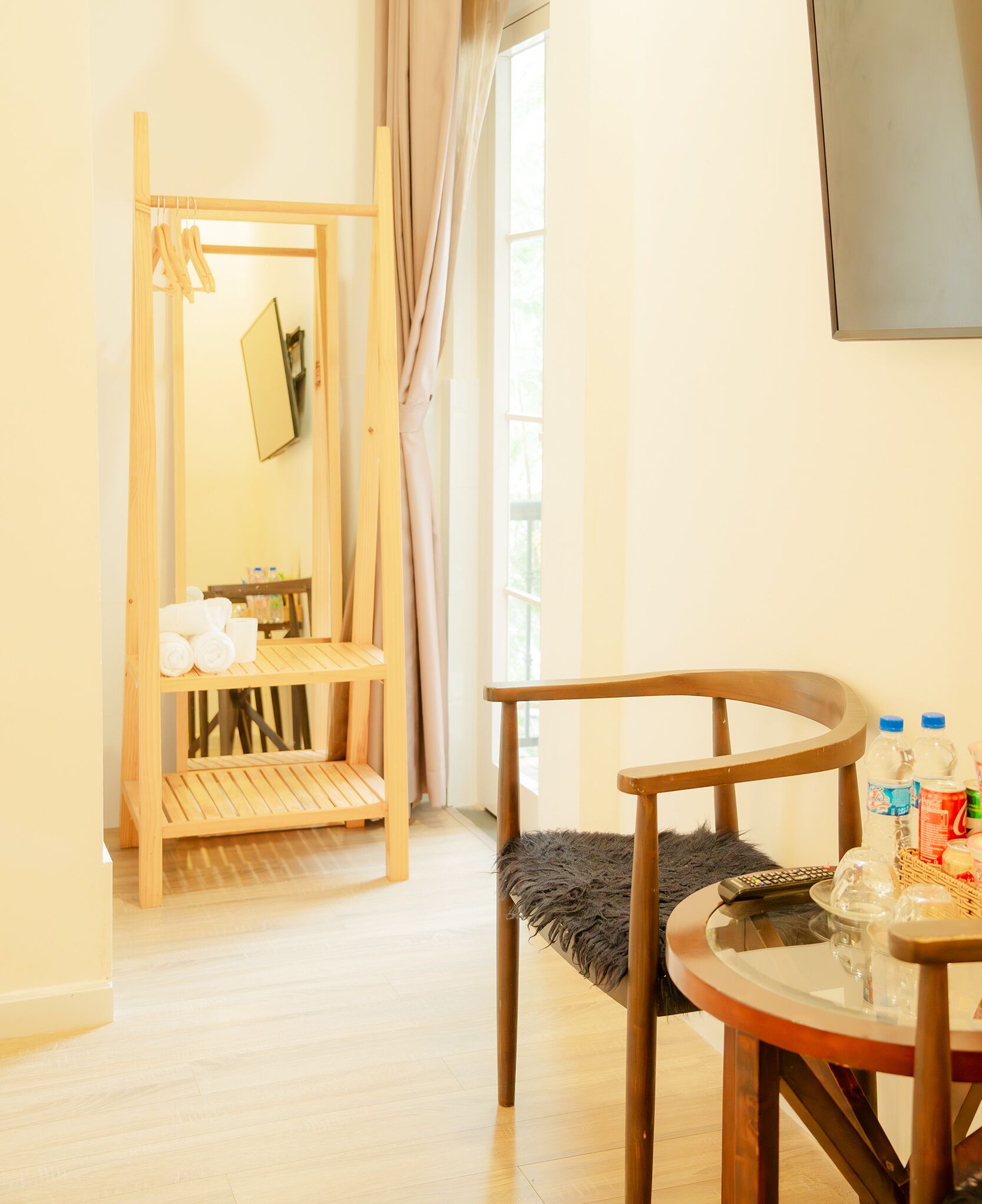A room with a wooden chair, a small round table with a glass top, a wooden shelf unit, and a mirror on the wall.