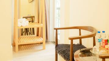 A room with a wooden chair, a small round table with a glass top, a wooden shelf unit, and a mirror on the wall.