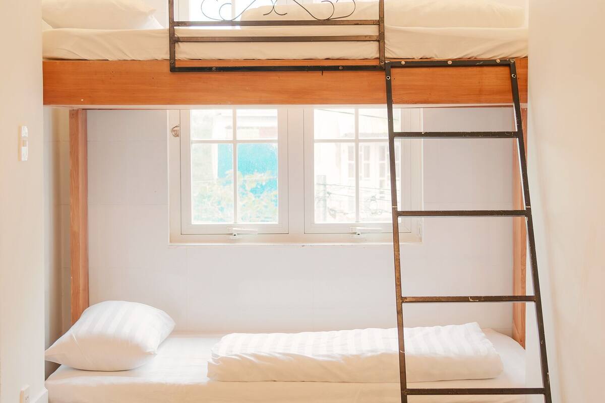 A bunk bed with a ladder, wooden floor, and a window with a view of buildings.