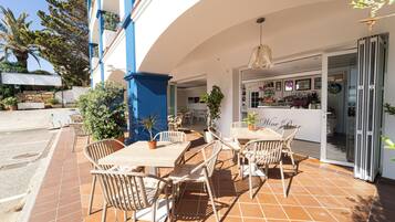 Un patio al aire libre con mesas y sillas, una zona de bar y plantas en macetas.