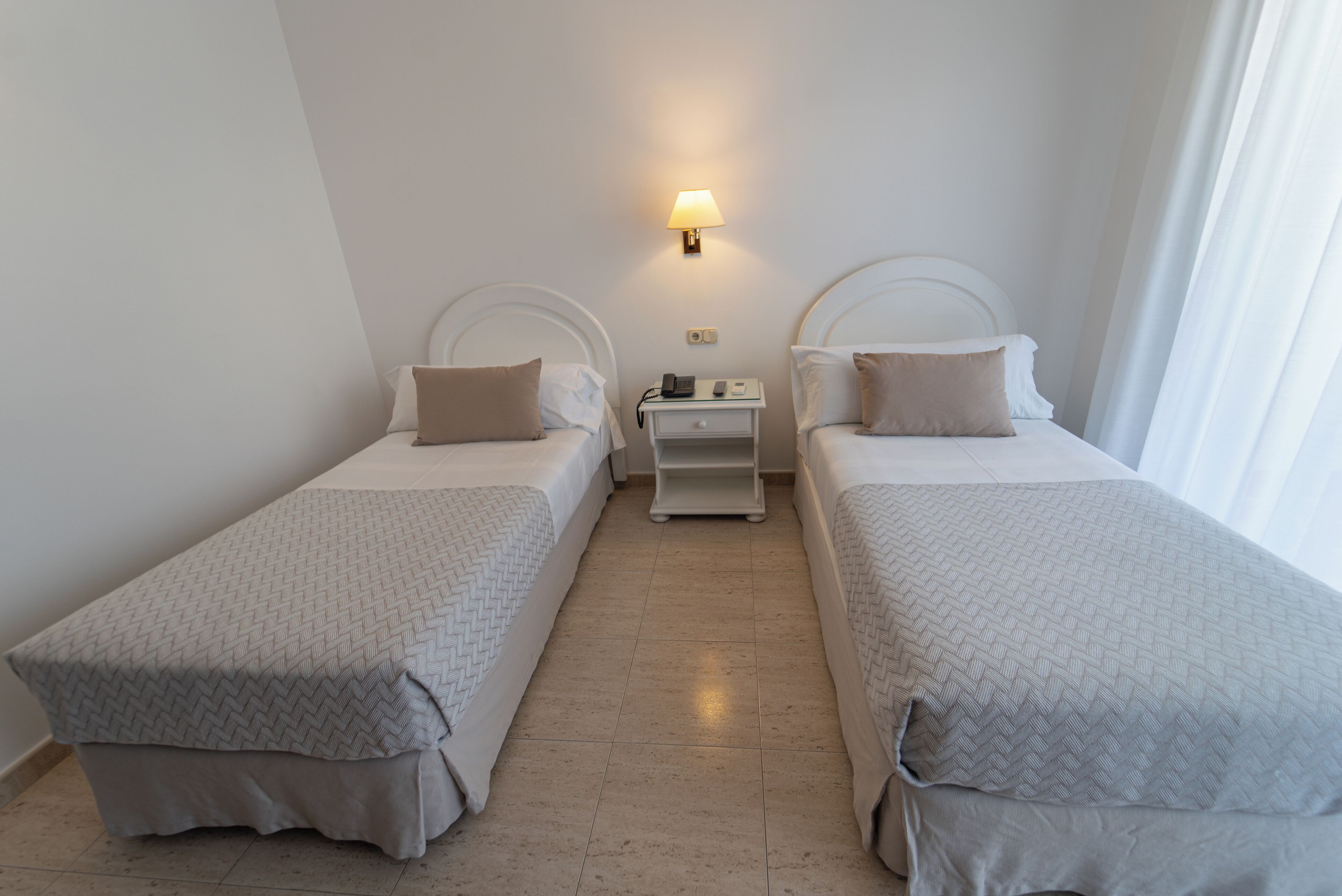 Ein Hotelzimmer mit zwei Einzelbetten, einem Nachttisch mit Lampe und einem kleinen Tisch.