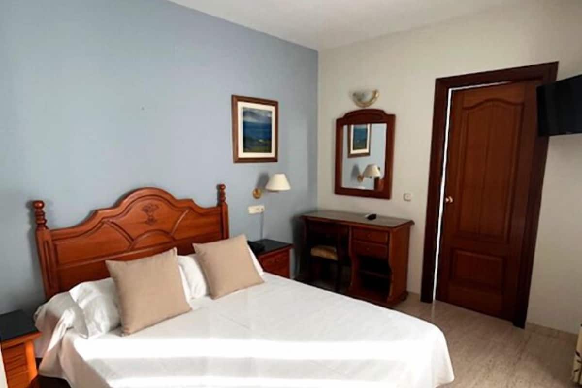 Un dormitorio con cama de madera, un escritorio, una silla, un espejo y una puerta.
