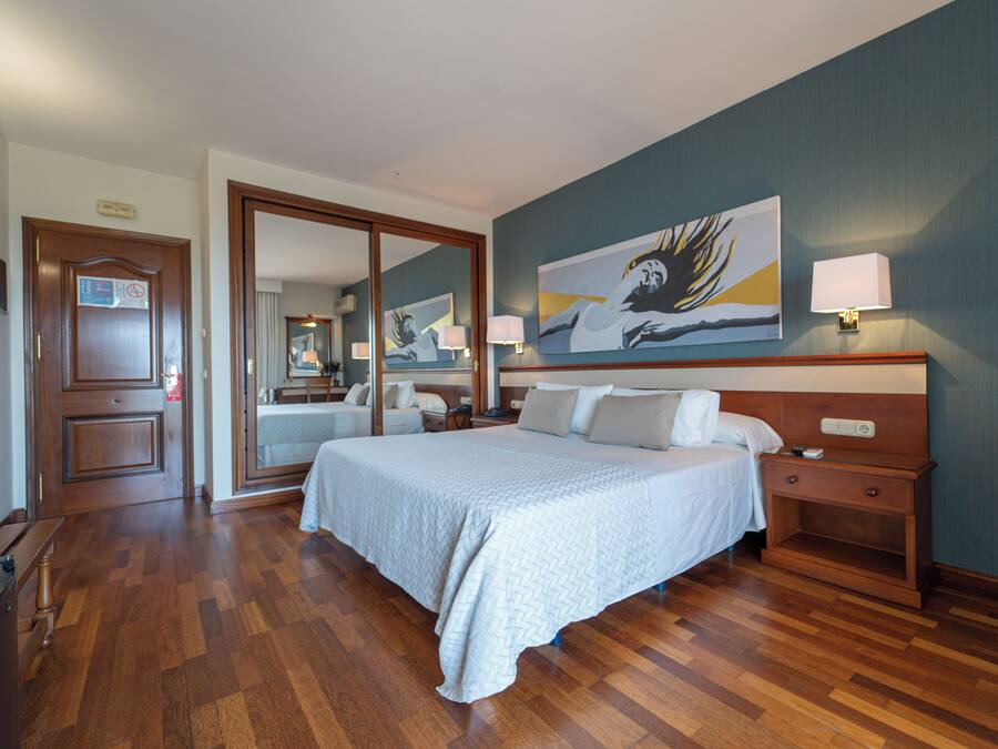 A hotel room with a large bed, a nightstand, a desk, and a painting on the wall.
