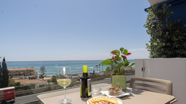A table with a glass of white wine, a bottle of olive oil, a plate of snacks, and a potted plant on a balcony overlooking the sea. - Hotel Piedra Paloma by Croma (Estepona)