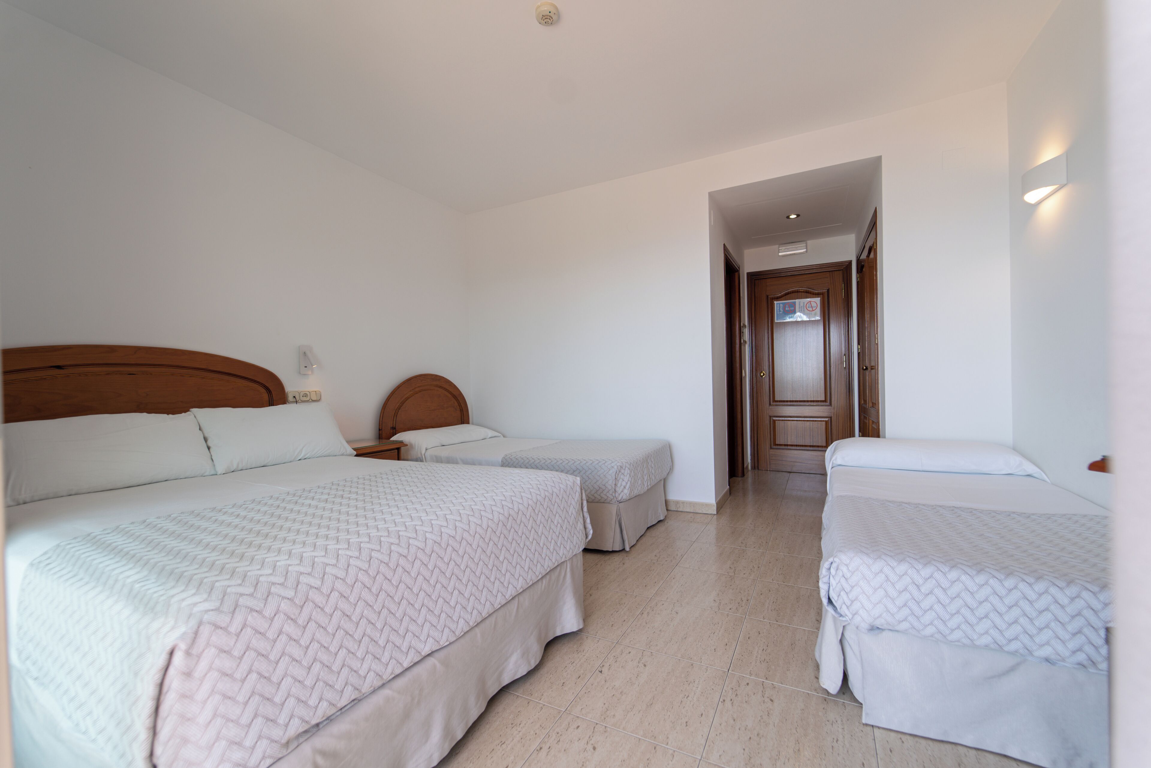 A hotel room with two single beds, a wooden headboard, a nightstand, and a door leading to another room.