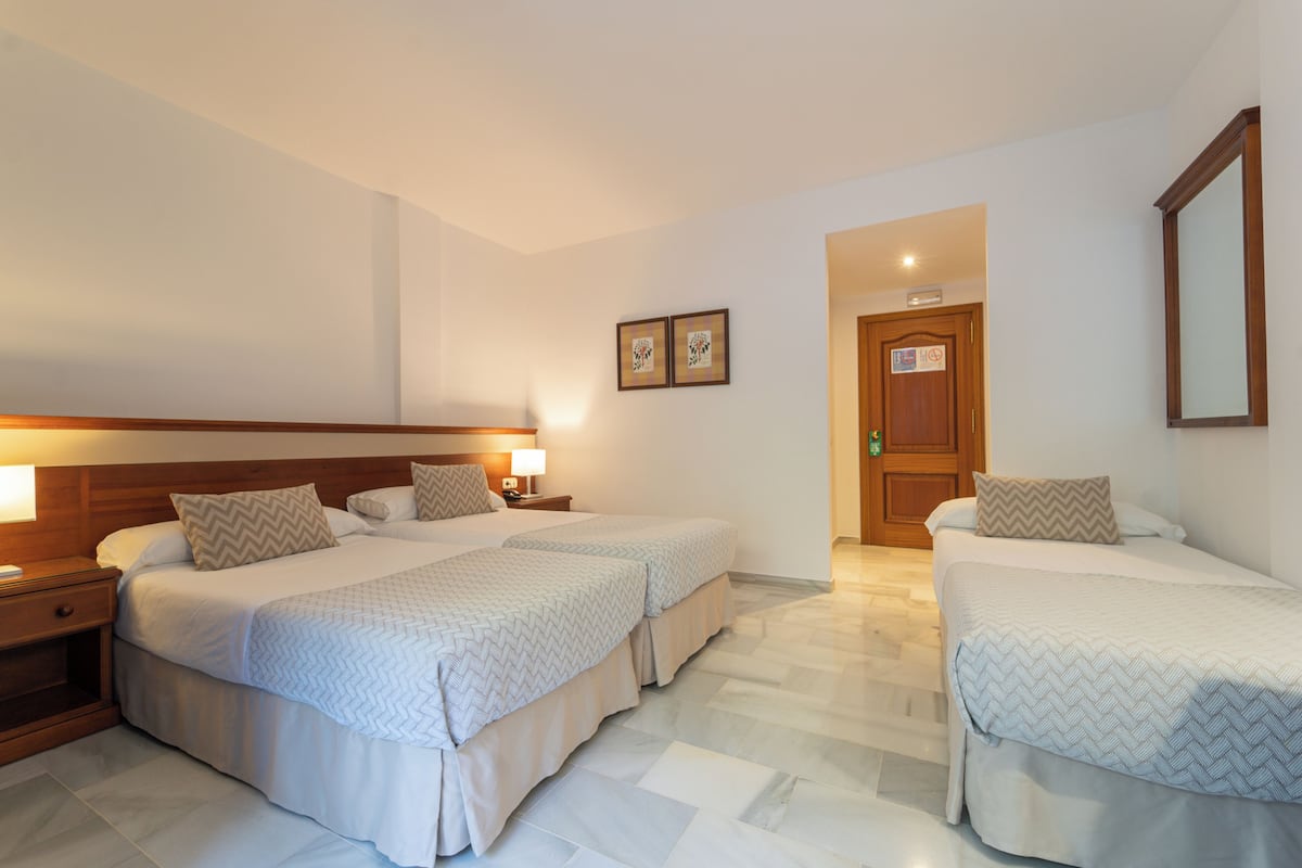 Habitación de hotel con dos camas, cabecero de madera, mesitas de noche con lámparas y una puerta con un letrero.
