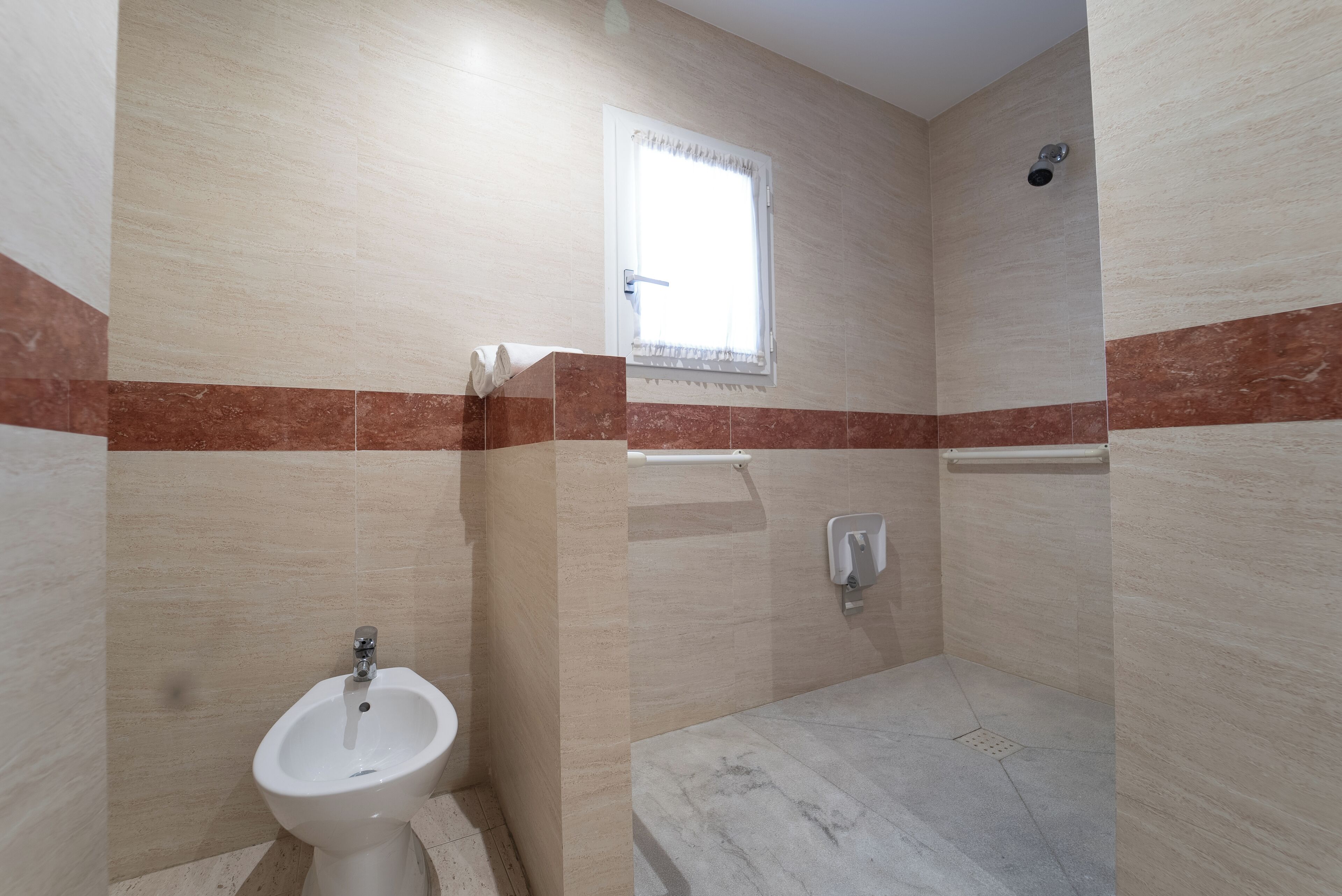 A bathroom with a bidet, a towel rack, and a window.