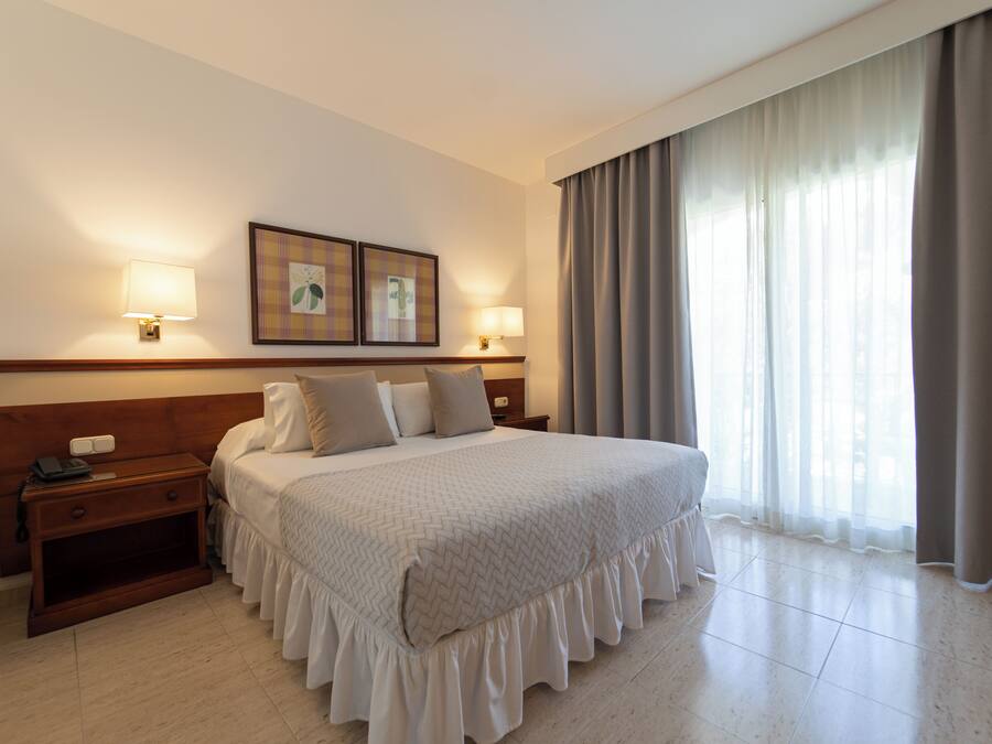 A hotel room with a large bed, two bedside lamps, a nightstand, and a window with curtains.