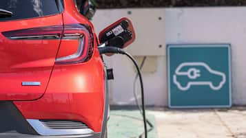 Un'auto elettrica rossa in fase di ricarica presso una stazione, con un segnale che indica il parcheggio per veicoli elettrici.