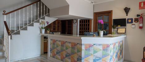 A reception area with a colorful geometric tile design, a wooden staircase, and a flat-screen TV mounted on the wall.