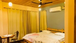 A room with a wooden ceiling, a bed with a floral bedspread, a desk with a chair, and an air conditioning unit on the wall. - Royal Guest House (Kala Amb)