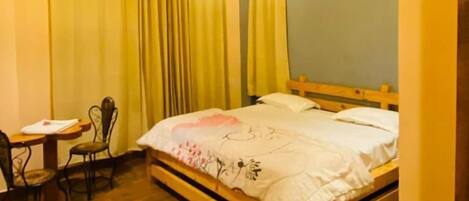 Una habitación con techo de madera, una cama con colcha estampada, un escritorio con silla y un equipo de aire acondicionado en la pared.