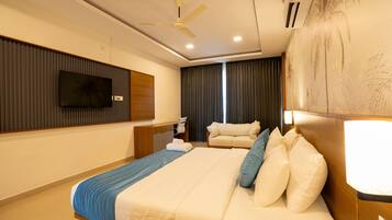 Una habitación de hotel con cama, escritorio, silla, televisor y ventilador de techo.