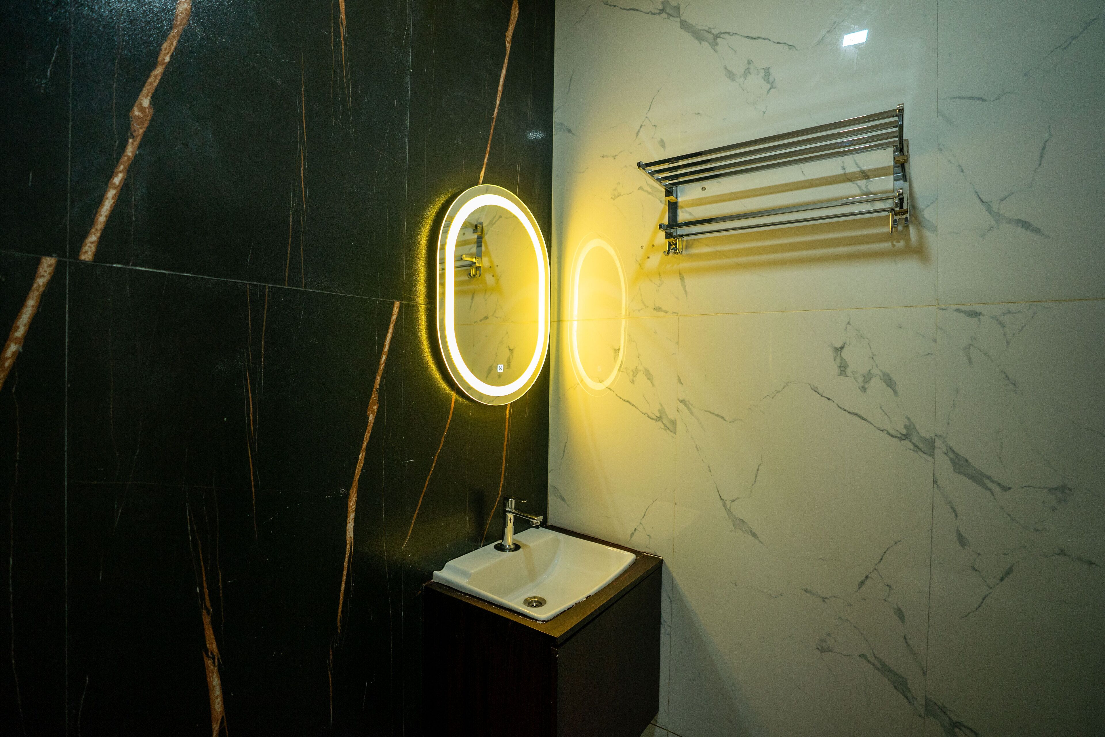 A bathroom with a sink, mirror, and towel rack against a marble wall.