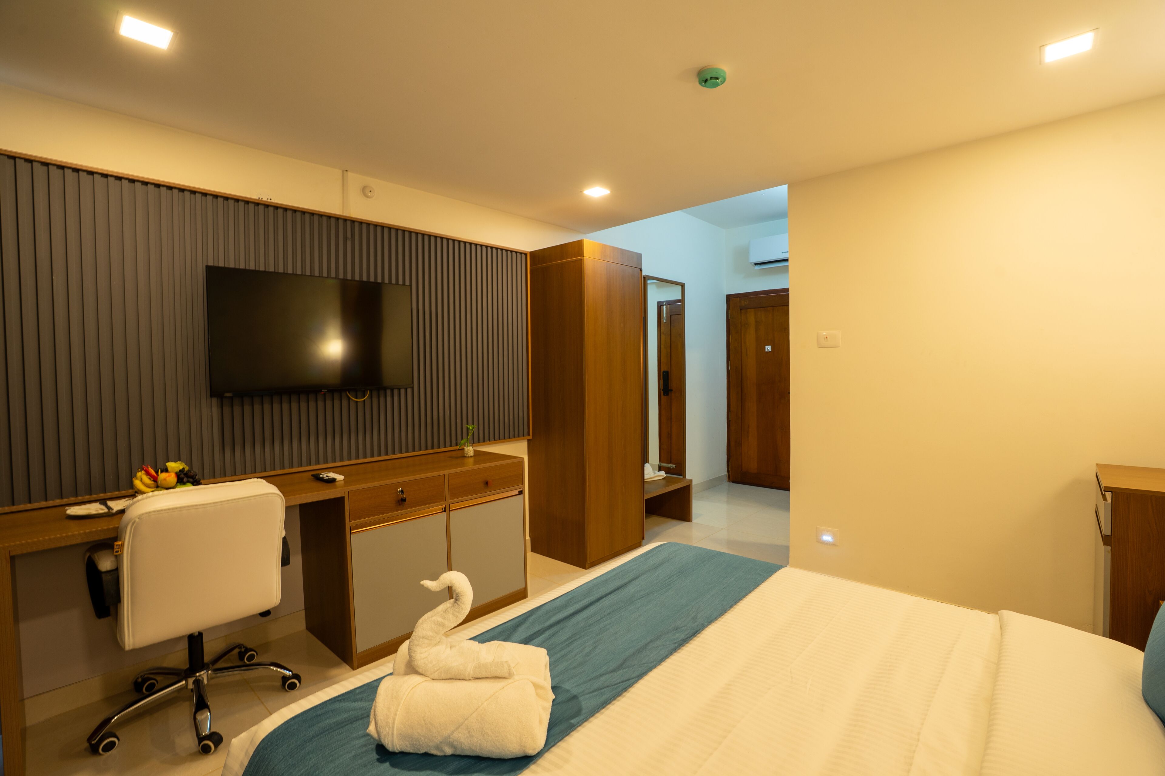Habitación de hotel con cama, escritorio, silla, televisión y baño a la vista.