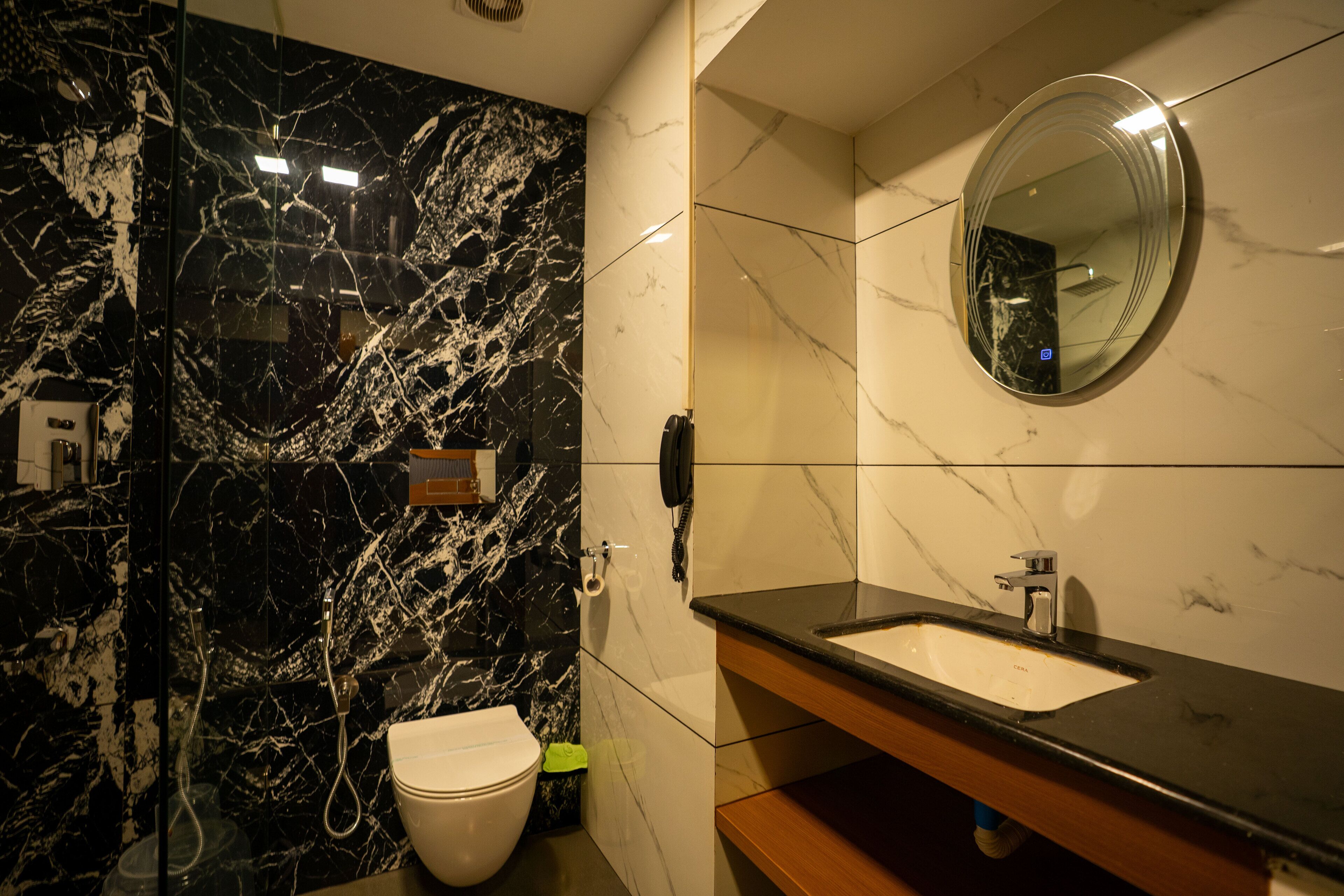 A modern bathroom with a black marble wall, a white toilet, a sink with a mirror above it, and a handheld showerhead.
