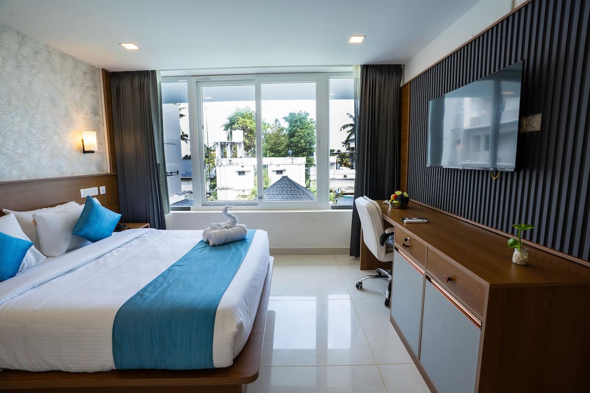 A hotel room with a large bed, a desk, a TV, and a view of the outside.