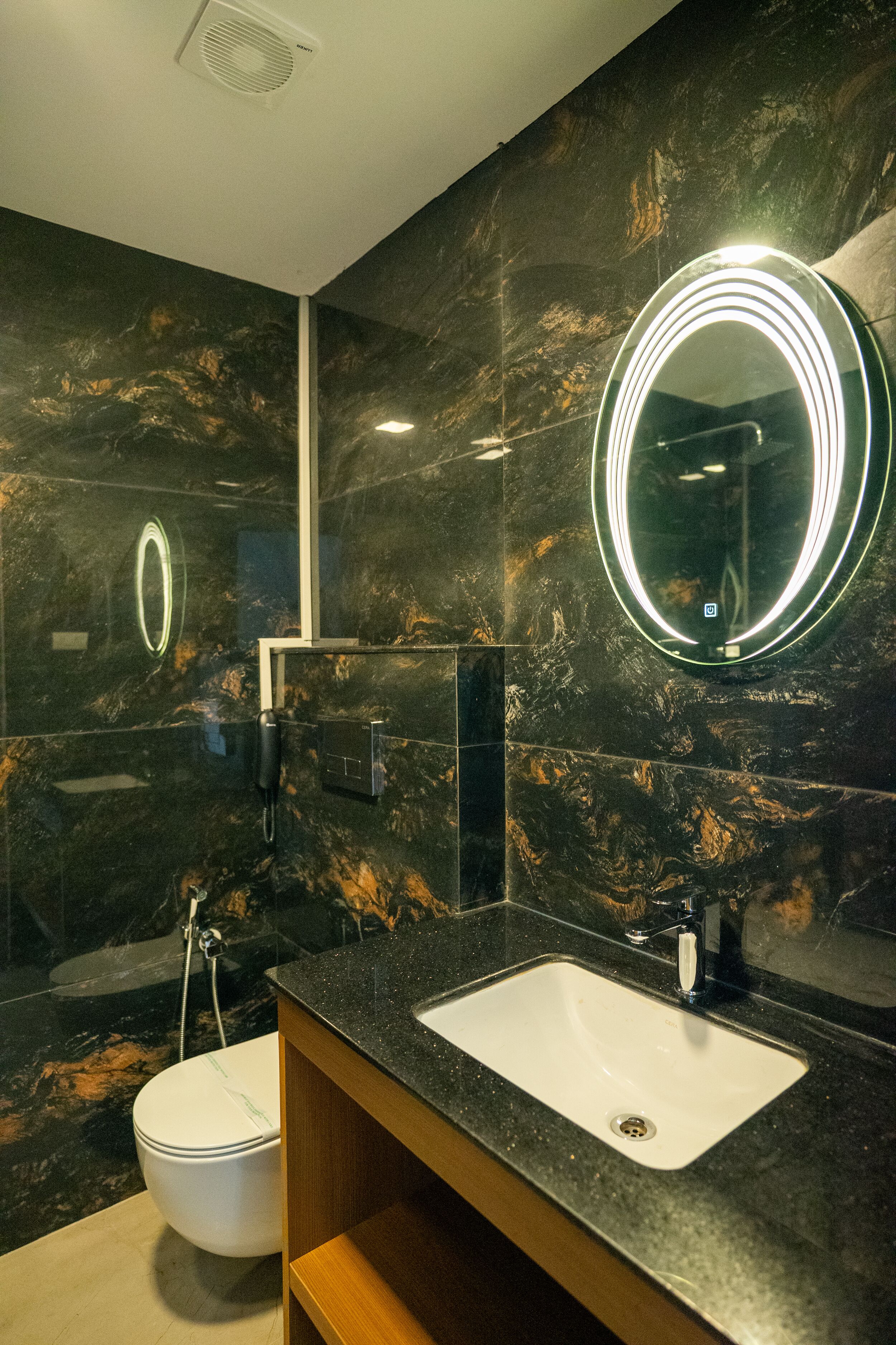 A modern bathroom with a marble wall, a white sink, and a mirror with illuminated lights.
