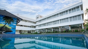Un hotel moderno con piscina, numerosi balconi e un murale raffigurante una spiaggia tropicale.