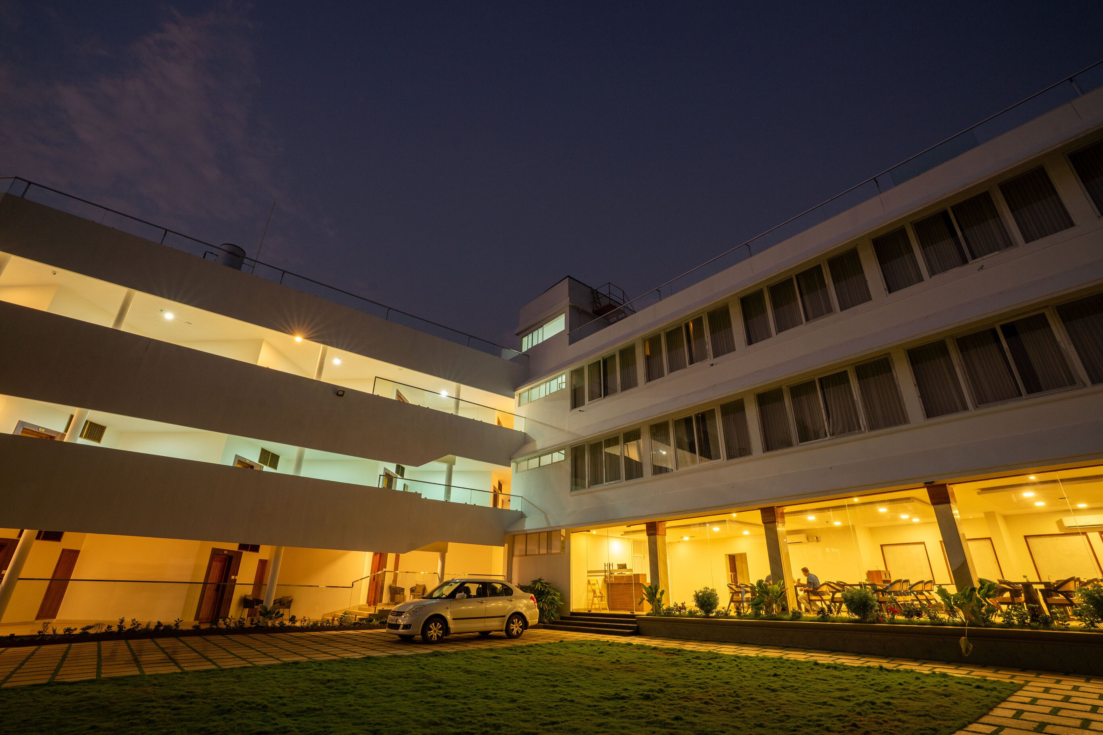 A modern multi-story building with a car parked in the driveway.