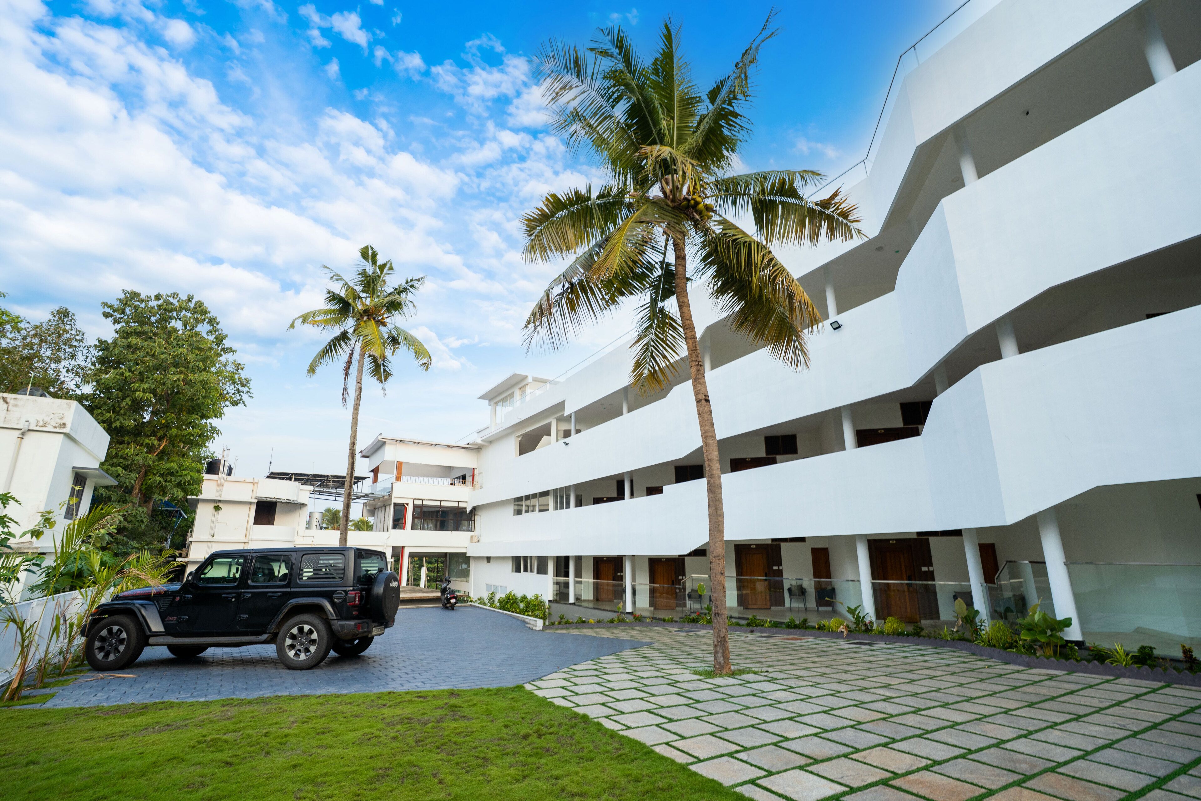 Un edificio moderno de varios pisos, un patio empedrado y palmeras.