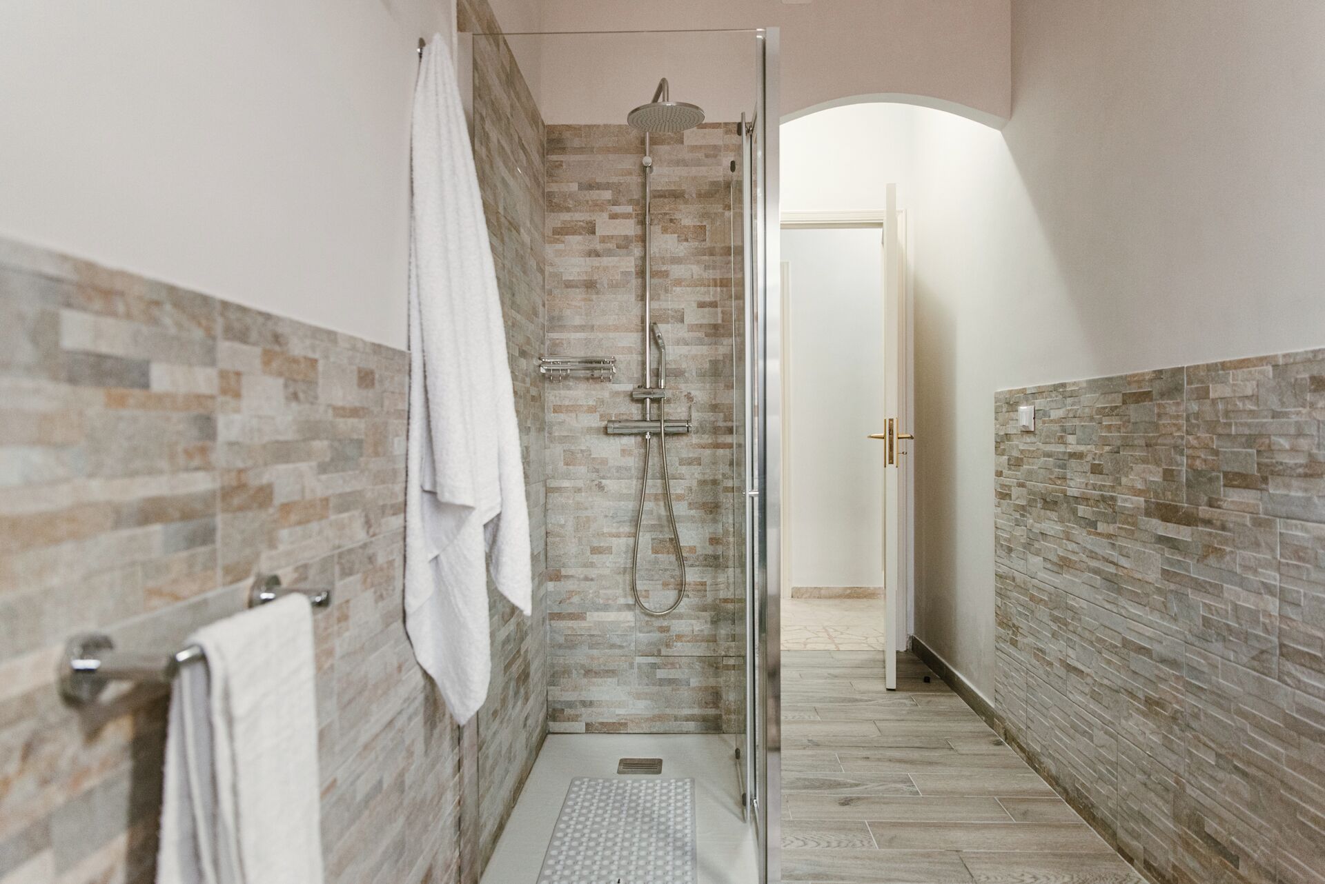Un baño moderno con cabina de ducha de vidrio, paredes revestidas de azulejos y un perchero visible.