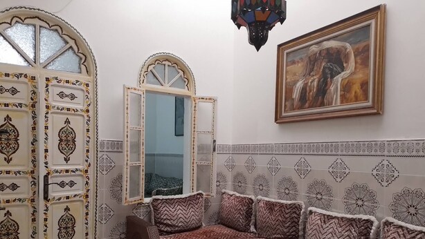 Een kamer met een traditioneel Marokkaans design, met een gestreept bankstel, een houten tafel en een decoratieve deur.