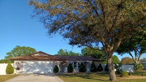 A single-story house with a covered porch, a driveway, and a large tree in the foreground. - Spacious 3-bedroom house with HOT TUB and MOVIE THEATRE 8 minutes from RACEWAY (Sebring)