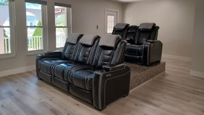 A room with a black leather sofa and two massage chairs, a stone accent wall, and large windows. - Spacious 3-bedroom house with HOT TUB and MOVIE THEATRE 8 minutes from RACEWAY (Sebring)